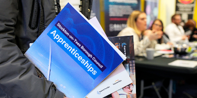 A close-up of somebody carrying an armful of apprenticeships documents - the one at the front has a picture of the Infinity Bridge on its cover and the words "Stockton-on-Tees Borough Council Apprenticeships".