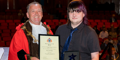 Photo with Mayor Councillor Faulks on the left and Alex Matthews on the right holding his Civic Award certificate in front of stage seating